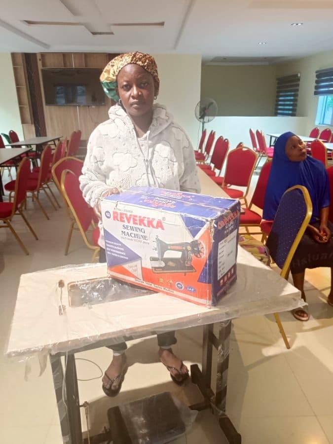 A participant stands with the boxed sewing machine and stand she received in the training hall